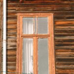 Close-up of a rustic wooden house facade featuring a vintage window with curtains.